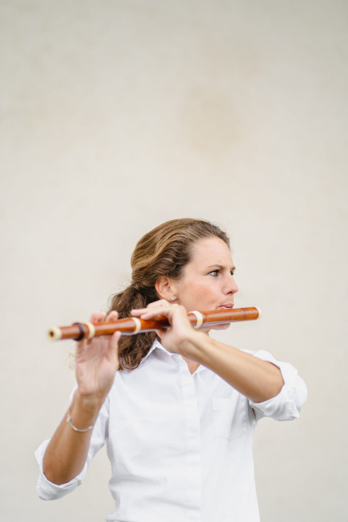 Charlotte Schmidt-Berger spielt Traversflöte vor grauer Wand