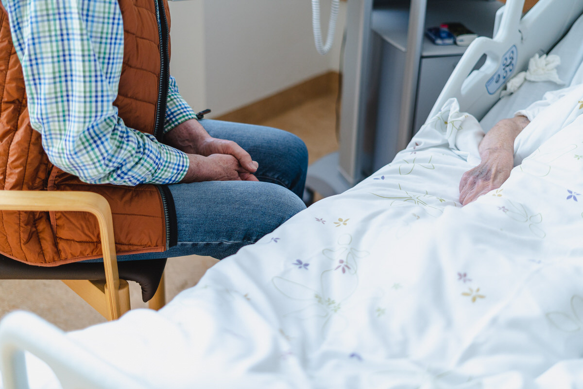 Mann sitzt an einem Krankenbett in der Palliativstation