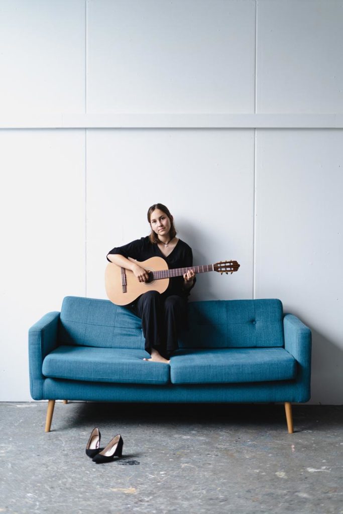 Musikerportrait Tina Wirsching sitzt mit Gitarre auf einem Sofa